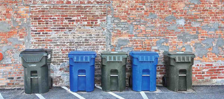 Five trash and recycle bins along a brick wall