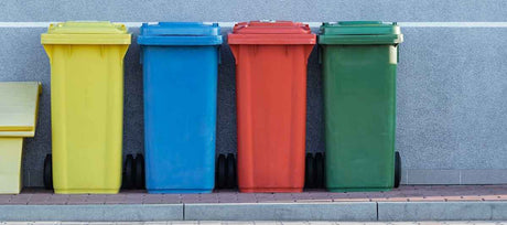 Green, red, blue, and yellow trash bins lined up against building